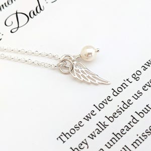 May include: A silver necklace with a delicate chain, featuring a small, openwork wing charm and a pearl. The necklace is displayed on a white surface with printed text that reads "Those we love don't go away".