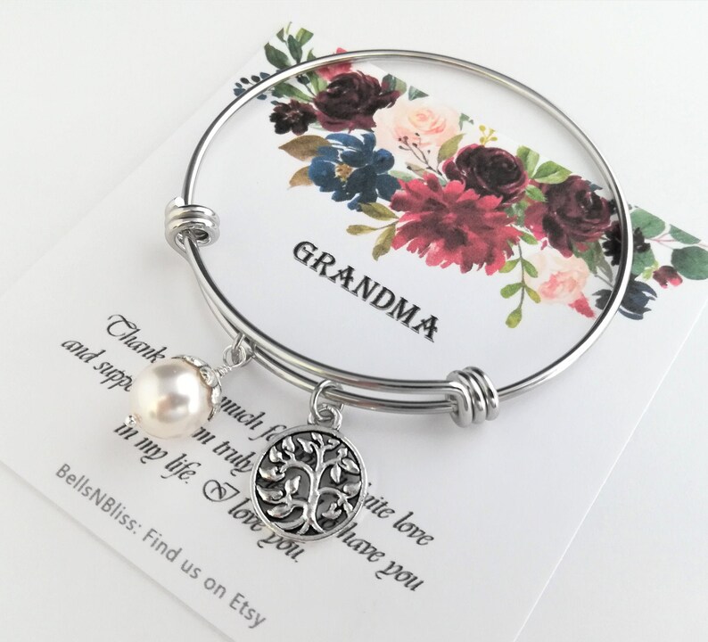 May include: A silver-toned bangle bracelet with a dangling pearl and a tree of life charm. The bracelet is displayed on a card with the word "GRANDMA" and a floral design in burgundy, navy, and blush tones. The card also has text.