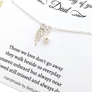 May include: A silver necklace with a wing charm and a pearl pendant. The necklace is displayed on a white card with the text "In memory of your Dad" and a poem about loved ones.