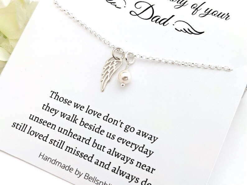 May include: A silver necklace with a wing charm and a pearl pendant. The necklace is displayed on a white card with the text "In memory of your Dad" and a poem about loved ones.