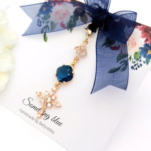 May include: A gold-toned charm featuring a deep blue square-cut crystal and a star-shaped crystal pendant, suspended from a dark blue sheer ribbon bow. The charm is attached to a white display card with the text Something blue Handmade by Bellsnbliss.