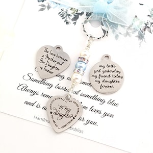 May include: A silver charm bracelet with three charms. The charms are heart-shaped and have engraved messages about the love between a mother and daughter. The charms are attached to a silver chain with pearl and blue bead accents.