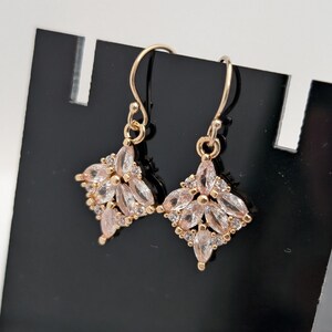 May include: A pair of gold-tone earrings with a square-shaped design featuring clear cubic zirconia stones.