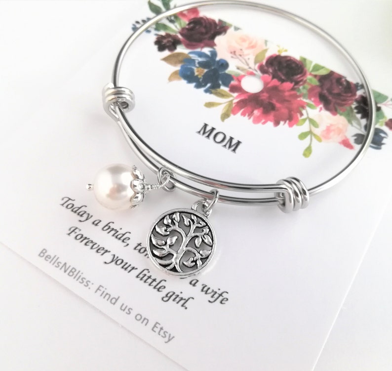 May include: A silver-toned bangle bracelet with a pearl charm and a tree of life pendant. The bracelet is displayed on a card with floral art and the word "MOM". The card also includes the text "Today a bride, to a wife, Forever your little girl."