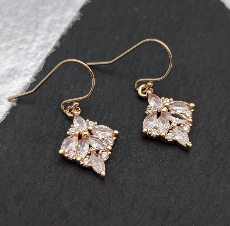 May include: A pair of gold dangle earrings with a cluster of clear, faceted stones in a floral design.