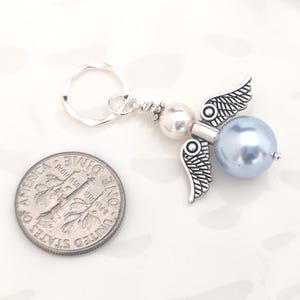 May include: A handmade angel keychain with a silver-tone metal angel wing charm and a light blue pearl bead body. The keychain includes a silver-tone split ring and a small white pearl bead. A U.S. dime is next to the keychain for size comparison.
