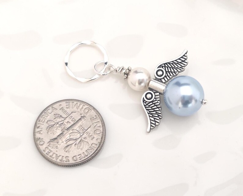 May include: A handmade angel keychain with a silver-tone metal angel wing charm and a light blue pearl bead body. The keychain includes a silver-tone split ring and a small white pearl bead. A U.S. dime is next to the keychain for size comparison.