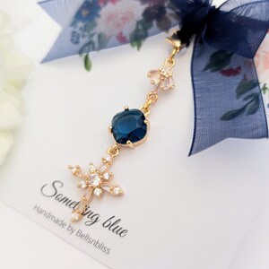 May include: A gold-toned charm featuring a deep blue square-cut stone and a star-shaped crystal pendant, suspended from a dark blue sheer ribbon. The charm is attached to a white card printed with the text Something blue Handmade by Bellsnbliss.