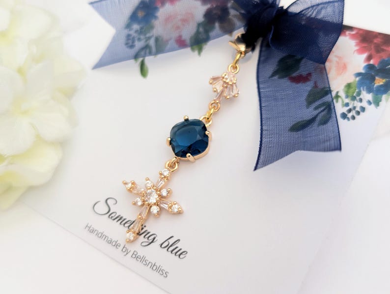 May include: A gold-toned charm featuring a deep blue square-cut stone and a star-shaped crystal pendant, suspended from a dark blue sheer ribbon. The charm is attached to a white card printed with the text Something blue Handmade by Bellsnbliss.