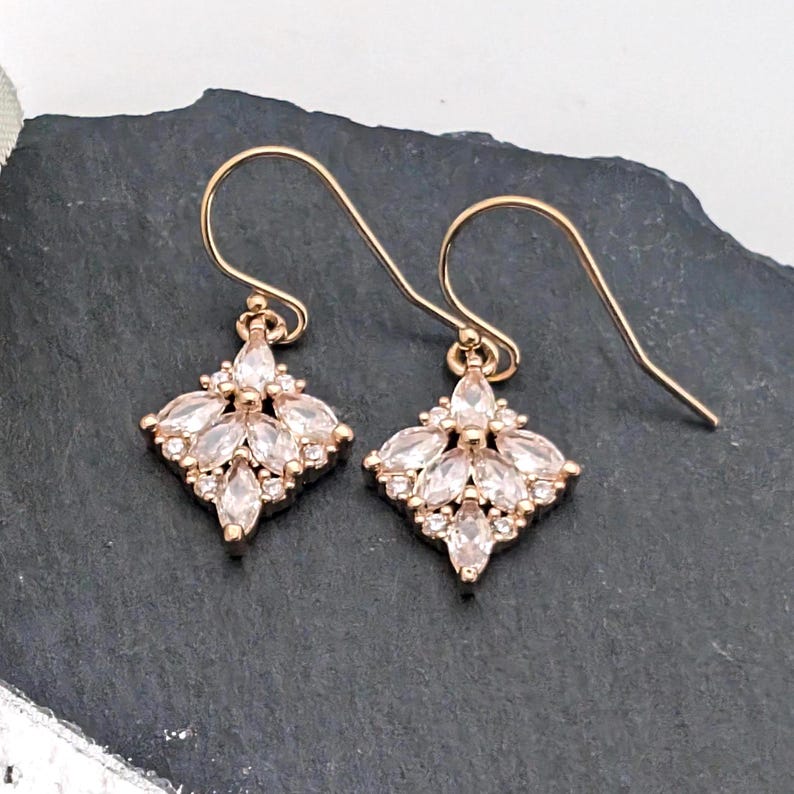 May include: A pair of rose gold earrings with a cluster of clear cubic zirconia stones in a diamond shape.