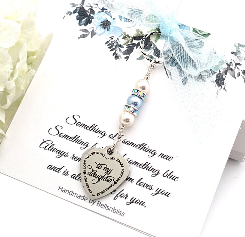 A delicate ‘Something Blue’ bridal bouquet charm gift for bride from Mom/Dad/parents — silver and blue wedding keepsake charm with steel heart-shaped to my daughter charm and a customizable message card reading ‘Something old, something new, something borrowed, something blue, always remember…’ ready to attach to a bride’s bouquet. Made by BellsNBliss and shown in a light blue ribbon tied gift box.