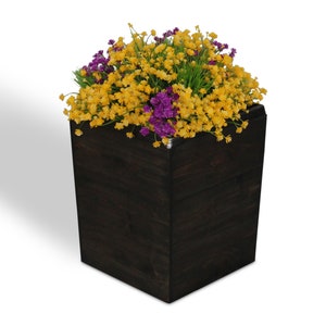 May include: A dark stained wooden planter box filled with yellow and purple flowers. The square planter has a modern design and is set against a white background. The flowers add a pop of color.