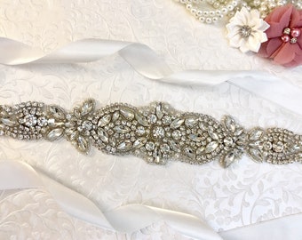 May include: A white satin ribbon with a crystal and pearl embellished bridal sash. The sash is decorated with clear rhinestones and pearls.