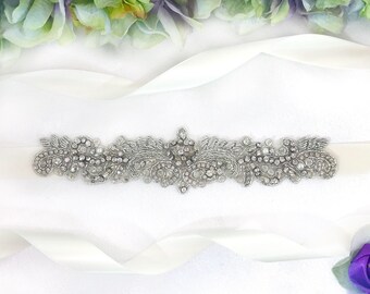 May include: A white satin ribbon with a silver beaded embellishment. The embellishment features a floral design with rhinestones.