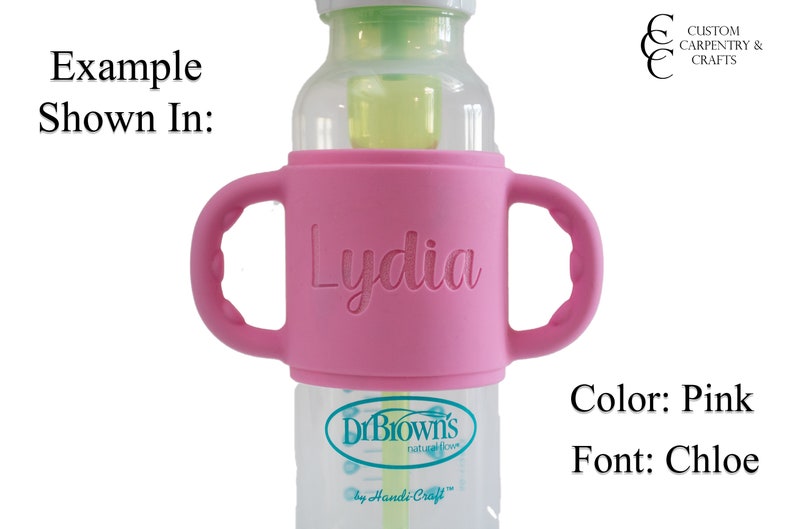 May include: Pink silicone bottle holder with two handles, personalised with the name "Lydia" in a Chloe font. The holder fits a Dr. Brown's bottle.