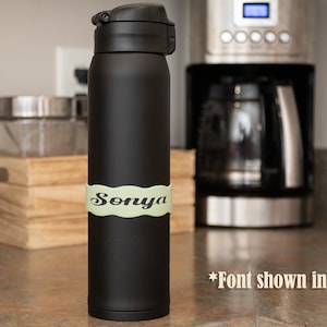May include: Black stainless steel water bottle with a green personalized label that says "Sonya". The font is shown in Reagan.