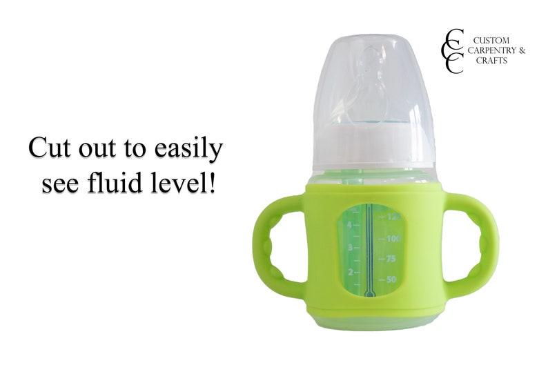 May include: A green silicone baby bottle with a clear glass insert and a white lid. The bottle has a handle on each side and a measurement scale on the side of the glass insert. The text "Cut out to easily see fluid level!" is visible in the image.