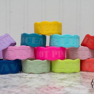 Puede incluir: Una pila de pulseras de silicona de colores con diferentes palabras en relieve, incluyendo "PURP", "PINK", "OCEAN", "YELLOW", "BLUE", "RED", "NAVY", "SAGE", "LIME" y "CORAL".