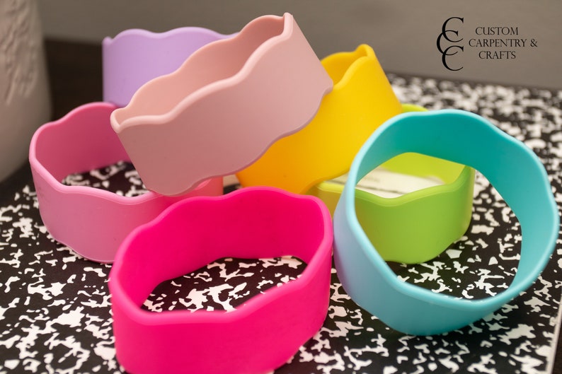 Puede incluir: Seis pulseras de silicona de colores con un borde festoneado. Las pulseras est&aacute;n apiladas una encima de la otra y est&aacute;n dispuestas en un patr&oacute;n de arco&iacute;ris. Las pulseras est&aacute;n sobre una superficie con un patr&oacute;n blanco y negro.