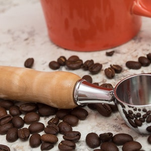 Peut inclure: Un gros plan d'une cuillère à café avec un manche en bois et une cuillère en métal argenté. La cuillère est entourée de grains de café sur une surface de couleur claire.