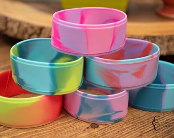 May include: A stack of six colourful silicone bracelets with a marbled pattern. The bracelets are stacked in a pyramid shape, with the largest bracelet at the bottom and the smallest bracelet at the top. The bracelets are all different colours, including pink, blue, green, and yellow.