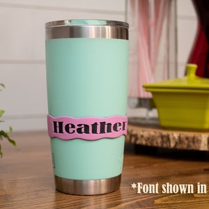 May include: A light green stainless steel tumbler with a pink personalized name band that says "Heather".