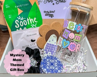 May include: A white gift box filled with a variety of items, including a face mask, eye mask, hair scrunchies, a cork coaster, a keychain, and a glass water bottle with a bamboo lid and a straw. The box is labeled "Mystery Mom Themed Gift Box". The water bottle has the words "Best Mom Ever" written on it in colorful letters.
