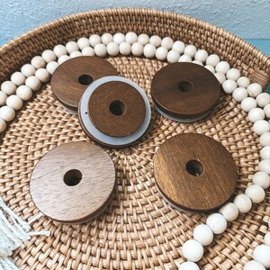 May include: Four wooden round bottle stoppers with a white ring around the top, sitting on a woven wicker tray with white beads around the edge.