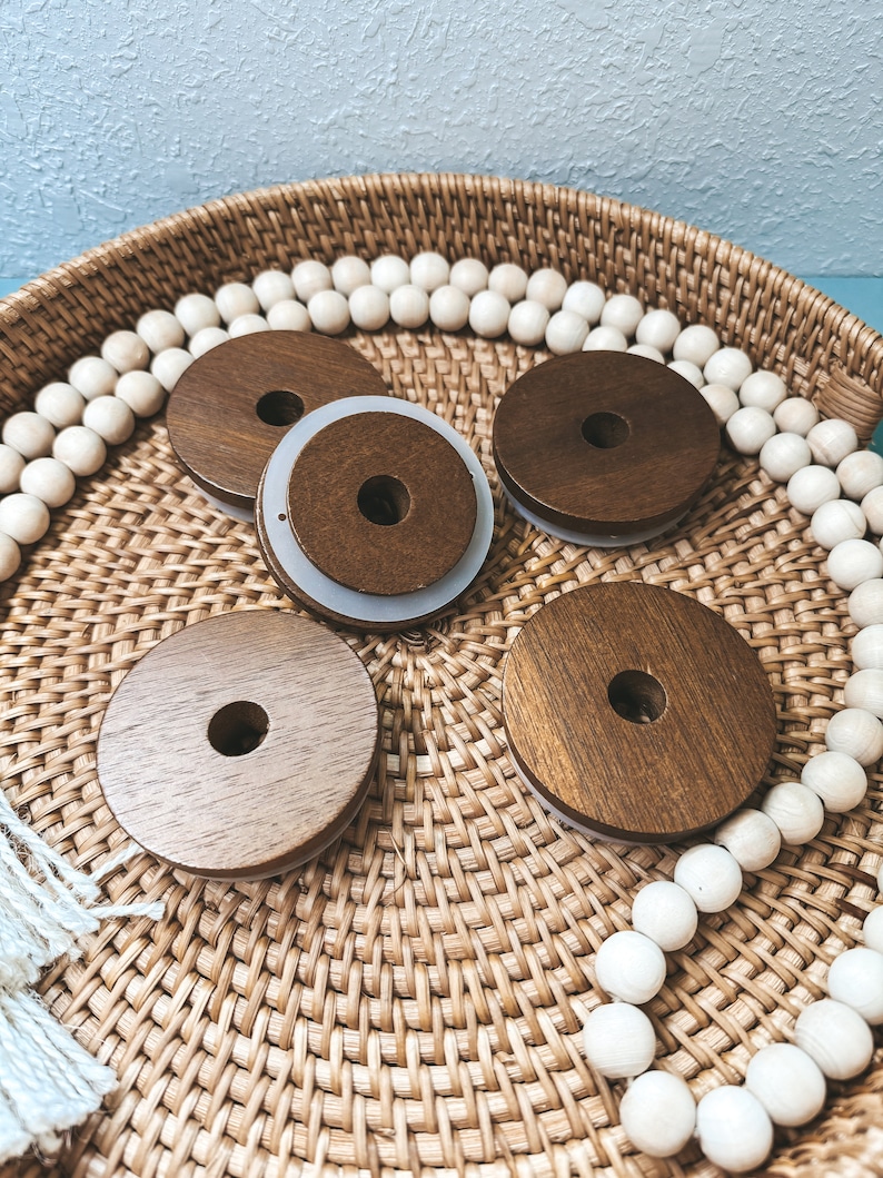 May include: Four wooden round bottle stoppers with a white ring around the top, sitting on a woven wicker tray with white beads around the edge.