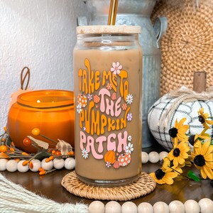 May include: A glass jar with a bamboo lid and a gold straw filled with a brown beverage. The jar has a graphic that says "Take Me To The Pumpkin Patch" with a pink and orange pumpkin design.