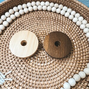 May include: Two wooden coasters, one light brown and one dark brown, with a hole in the center. The coasters are on a woven wicker tray with white wooden beads around the edge.