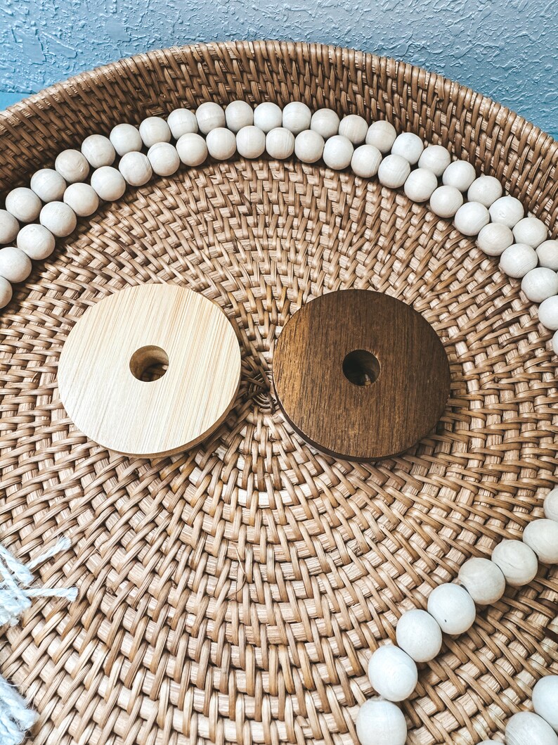 May include: Two wooden coasters, one light brown and one dark brown, with a hole in the center. The coasters are on a woven wicker tray with white wooden beads around the edge.