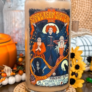 May include: A glass tumbler with a bamboo lid, featuring a colorful graphic of the Sanderson Sisters from the movie "Hocus Pocus." The design includes the text "Sanderson Sisters Back From The Dead" and "All Hallows Eve."