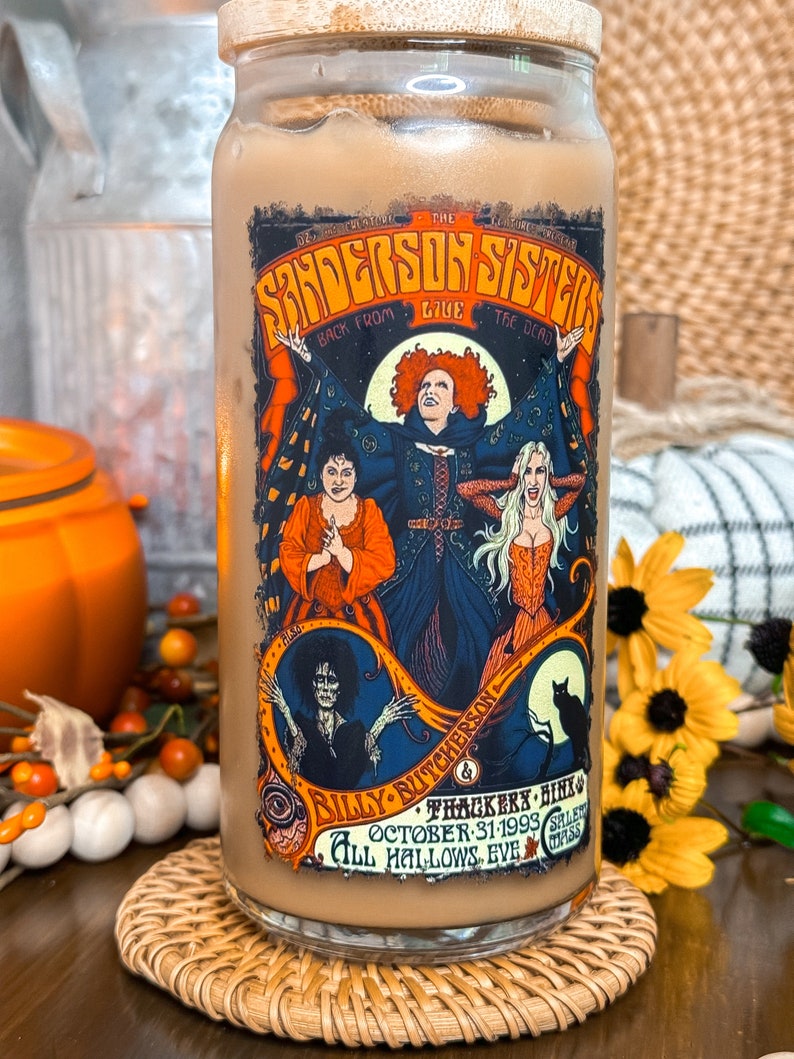 May include: A glass tumbler with a bamboo lid, featuring a colorful graphic of the Sanderson Sisters from the movie "Hocus Pocus." The design includes the text "Sanderson Sisters Back From The Dead" and "All Hallows Eve."