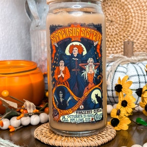 May include: A glass tumbler with a bamboo lid and a black straw, featuring a colorful graphic of the Sanderson Sisters from the movie "Hocus Pocus." The design includes text and illustrations, perfect for Halloween.