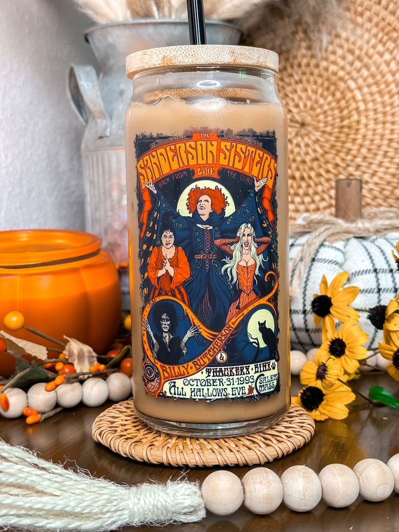 May include: A glass tumbler with a bamboo lid and a black straw, featuring a colorful graphic of the Sanderson Sisters from the movie "Hocus Pocus." The design includes text and illustrations, perfect for Halloween.