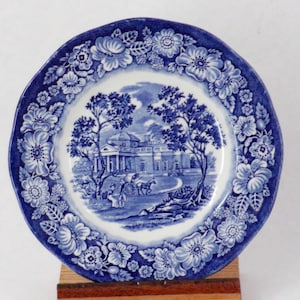 Puede incluir: Plato de porcelana azul y blanco con un borde floral y una escena de una casa con árboles y un carruaje en el centro.
