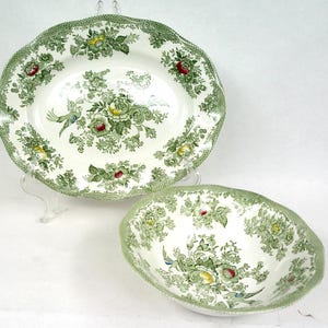 Pode incluir: Uma travessa oval e uma tigela redonda a condizer, feitas de cerâmica cor de creme. Ambas as peças apresentam um padrão detalhado de transferência verde com ramos de flores, folhagem em espiral e pássaros, com pequenos toques de amarelo e vermelho.