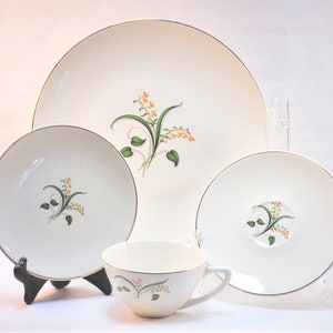 Puede incluir: Juego de vajilla de porcelana blanca con diseño floral en tonos naranja y verde. El conjunto incluye un plato grande, un plato más pequeño, un platillo y una taza de té, todos con ribete dorado. El patrón floral se repite.