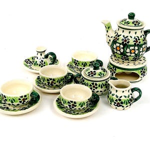May include: A miniature ceramic tea set featuring a cream-coloured base with hand-painted green leaves and orange flower patterns. The set includes a teapot on a warmer, a lidded sugar bowl, a creamer, four teacups with saucers, and a candlestick.