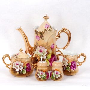 May include: A porcelain tea set with a gold trim and floral design. The set includes a teapot, creamer, sugar bowl, and two salt and pepper shakers.