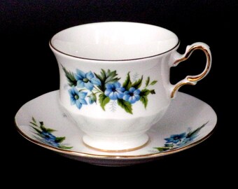 May include: A white teacup and saucer set with a blue floral pattern. The cup has a gold rim and a gold handle. The saucer also has a gold rim.