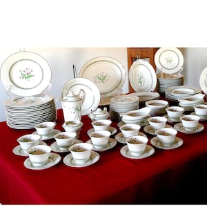 May include: A complete vintage white porcelain dinnerware set with a floral design. The set includes plates, cups, saucers, a teapot, and serving dishes. Each piece features a green trim and a delicate floral pattern in the center.