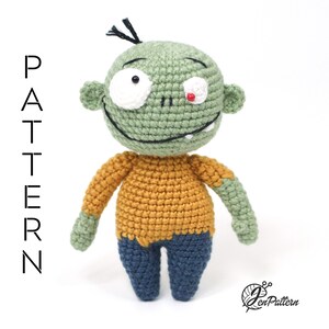 K&ouml;nnte beinhalten: Gr&uuml;ne geh&auml;kelte Zombie-Amigurumi-Puppe mit gelbem Shirt und blauer Hose. Die Puppe hat ein wei&szlig;es Auge und ein rotes Auge.