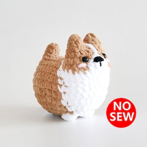Puede incluir: Un juguete de peluche de crochet marrón y blanco con forma de perro. El juguete tiene ojos negros y una nariz negra. El juguete está etiquetado como "NO SEW".