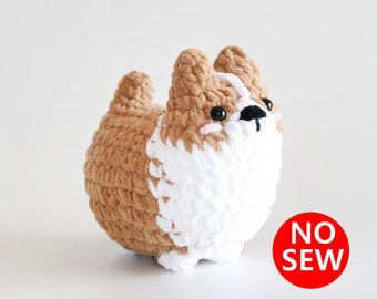 May include: A brown and white crocheted plush toy shaped like a dog. The toy has black eyes and a black nose. The toy is labeled "NO SEW".