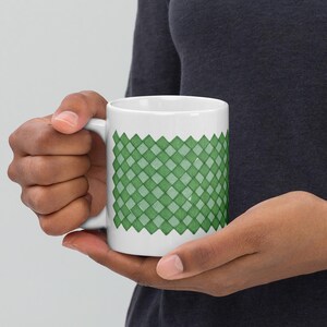 May include: A white ceramic mug with a green diamond pattern design. The mug has a handle and is suitable for hot or cold beverages.