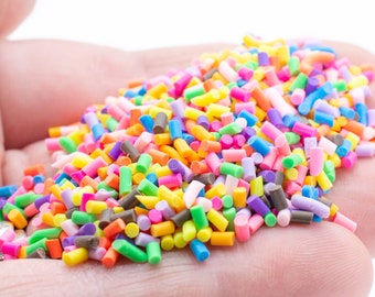 Op de afbeelding: Een close-up van een hand die een grote hoeveelheid kleurrijke sprinkles vasthoudt. De sprinkles zijn een mix van roze, blauw, groen, geel, oranje en paars.