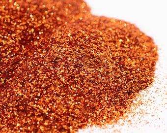 May include: A close-up of a pile of orange glitter. The glitter is very fine and has a metallic sheen.