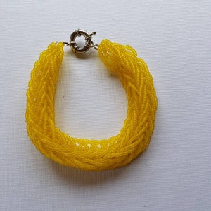 May include: A yellow beaded bracelet with a silver clasp. The bracelet is made of many small beads woven together in a braided pattern.